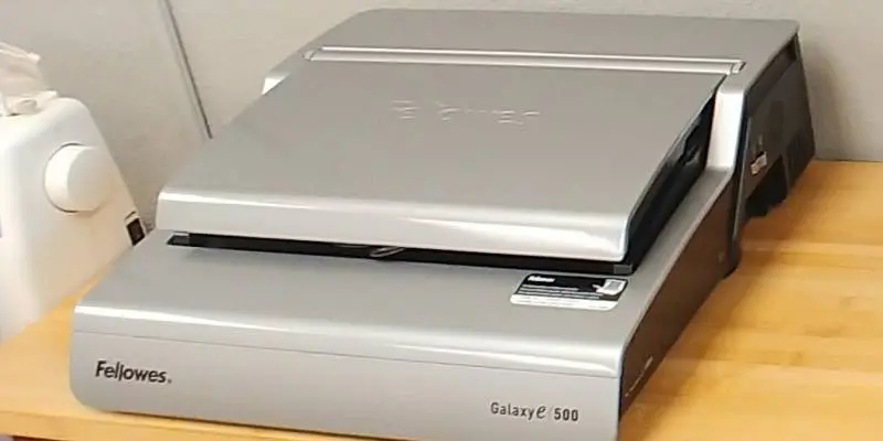 A Silver book-binding machine sits atop a wooden table.